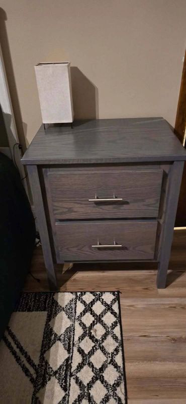 A gray wooden nightstand with two drawers and a white lamp on top.