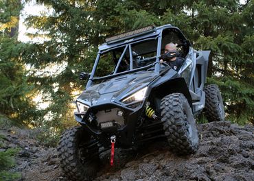 Photo of black off-road vehicle in woods with sun shining through trees behind it.