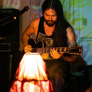 Man with long hair playing electric guitar in dimly lit room.