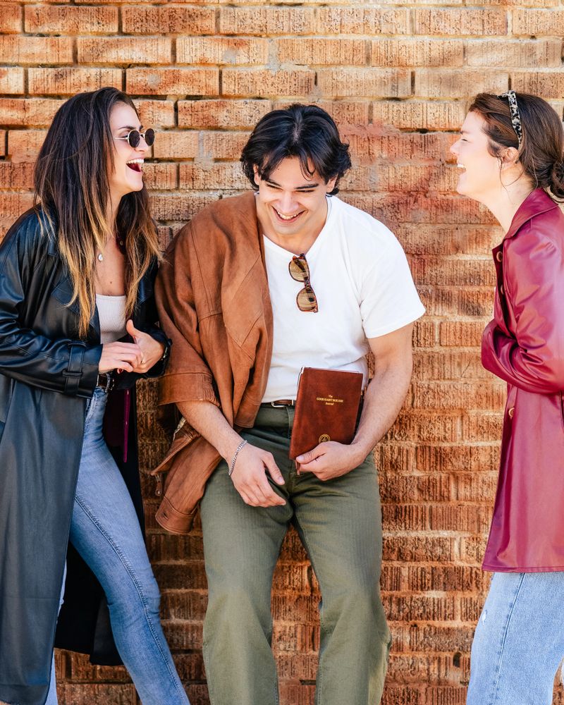 Three friends laughing joyfully against a brick wall.