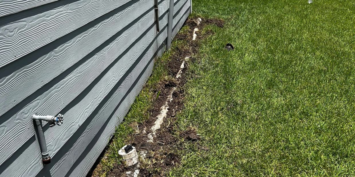 Exposed underground pipe line along a house wall and grass lawn.