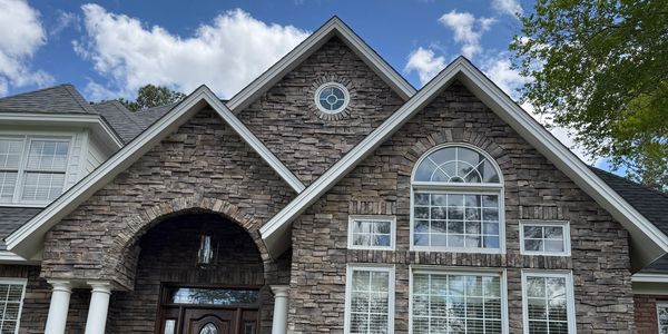 Stone facade house with arched windows and wooden door under a blue sky.