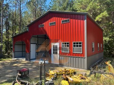 Red and gray metal barn surrounded by trees.