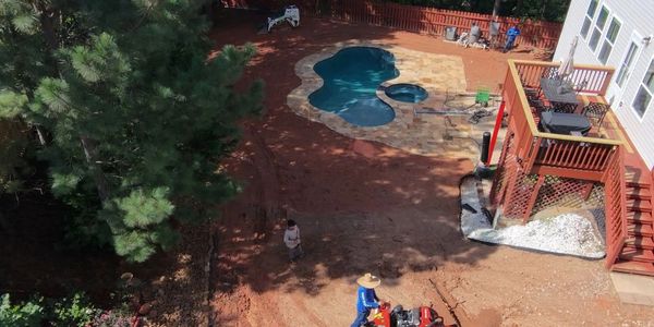 Backyard landscaping with a pool and workers operating machinery.