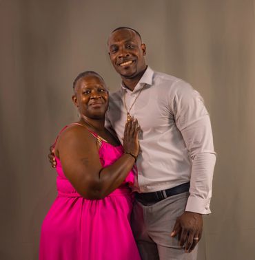 A couple smiles warmly, embracing each other against a plain background.