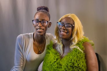Two smiling women wearing glasses pose together against a neutral backdrop.