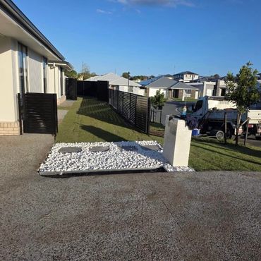 Modern house exterior with black fence and white stone landscaping under clear blue sky.
