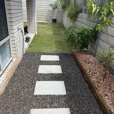 Modern backyard with stepping stones, gravel, and green plants along a wooden fence.
