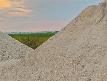 Two large gravel piles with green fields and a sunset in the background.