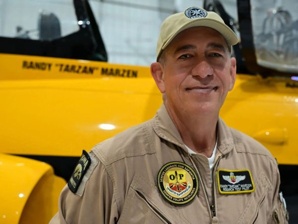 Pilot in uniform standing in front of a yellow aircraft.