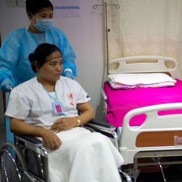 Patient in wheelchair being pushed by healthcare worker in hospital.