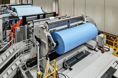 Industrial machine processing a large blue paper roll.