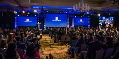 A large audience attends a corporate event in a grand hall with blue lighting.