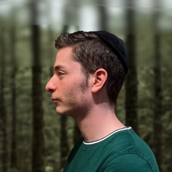 Profile of a young man wearing a kippah in a forest.
