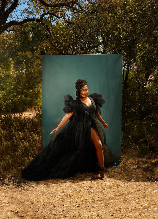 Woman in a dramatic black gown poses outdoors against a green backdrop.