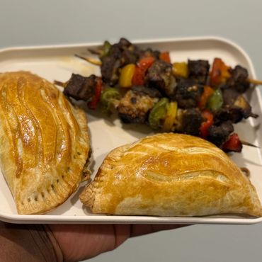 Plate with two baked empanadas and two skewers of grilled meat and vegetables.