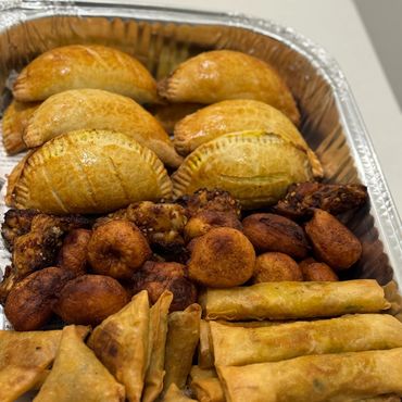 Tray of assorted fried snacks, including samosas, spring rolls, and empanadas.