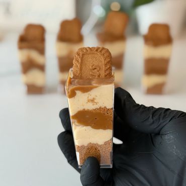 Hand holding layered dessert with biscuit on top, more in background.