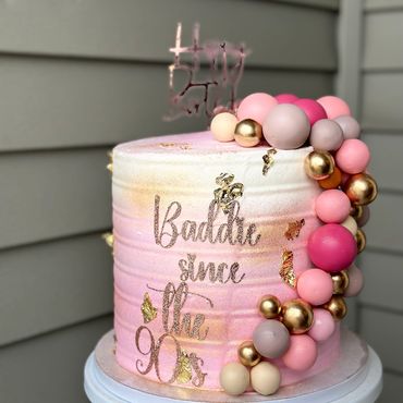 Pink and gold cake with "Baddie since the 90's" decoration and colorful spheres.