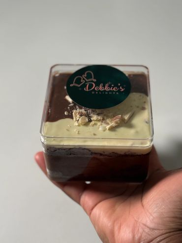 Hand holding a layered dessert from Debbie's Delights in a clear container.