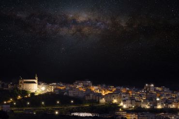 Starry night sky over a softly lit village with a prominent church.