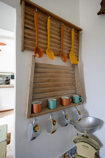 Wooden kitchen rack with orange and yellow utensils and colorful cups.
