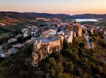 A historic fortress atop a hill overlooking a quaint village at sunset.