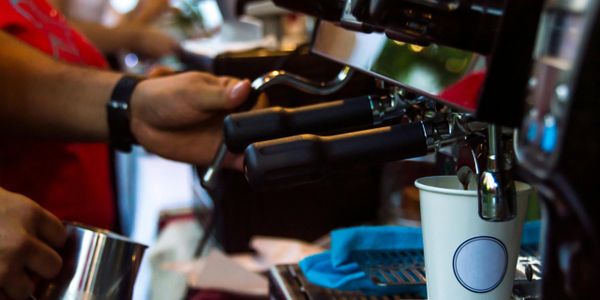 Barista preparing espresso using an espresso machine with a paper cup.