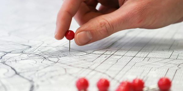 Hand placing a red pushpin on a detailed map.