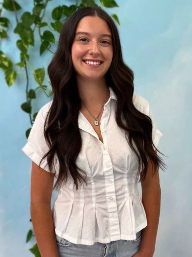 Smiling young woman with long dark hair in white shirt.