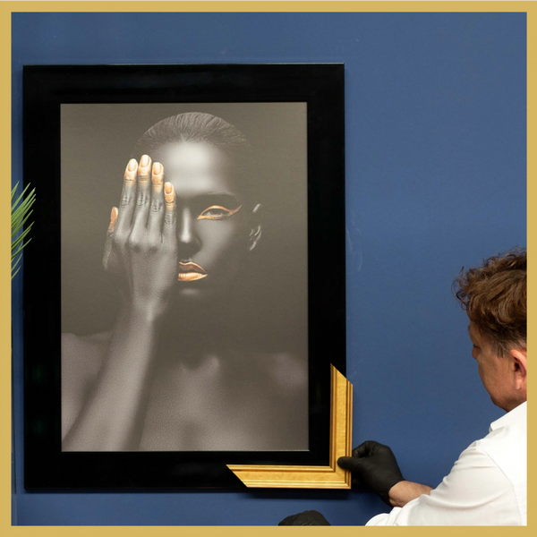 Artysta Włodzimierz Zapart dopasowujący złotą ramę do obrazu.