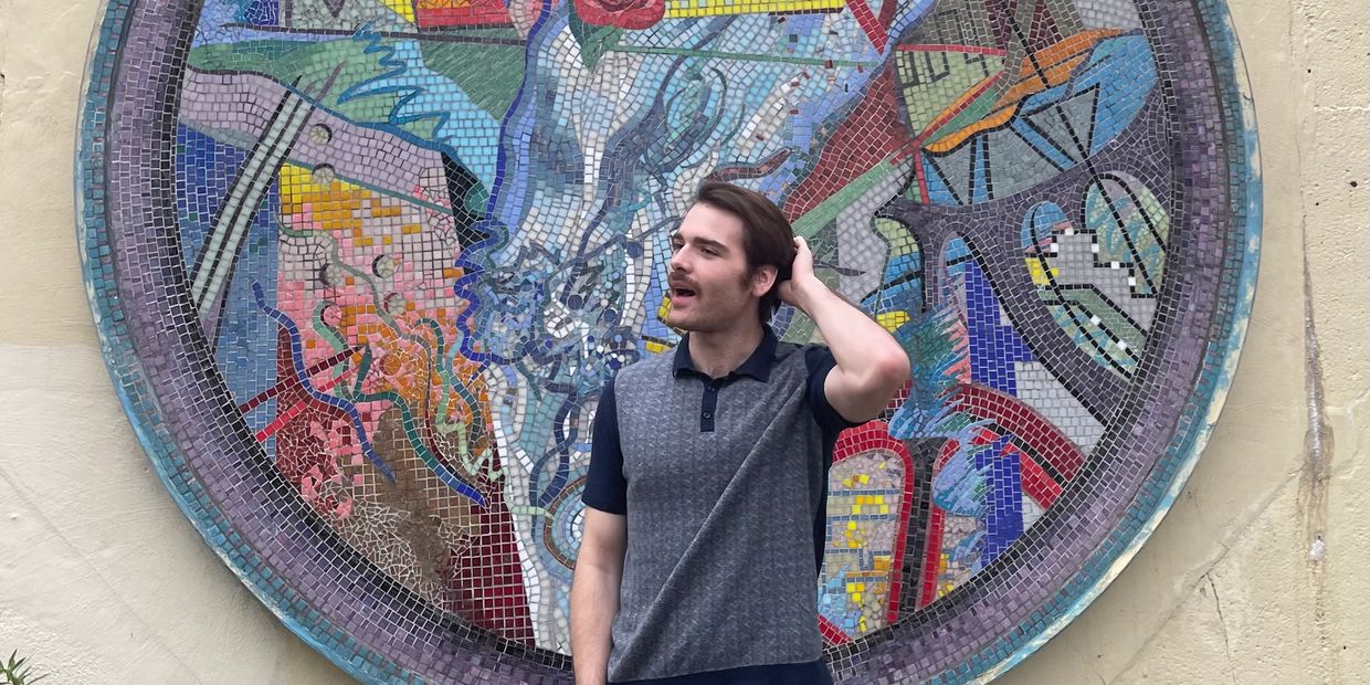 Man standing in front of a colorful circular mosaic wall art.