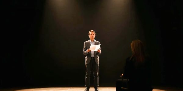 Man in suit standing on stage reading paper.