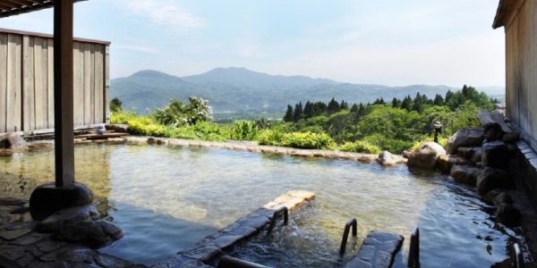Outdoor hot spring bath with mountain views under a clear sky.