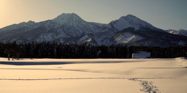 Snow-covered field with mountain backdrop at sunset.