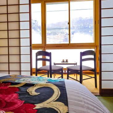 Cozy room with floral bedspread and two chairs by a window with mountain view.
