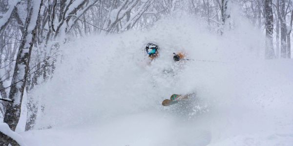 Skier bursts through deep powder snow in a forested winter landscape.