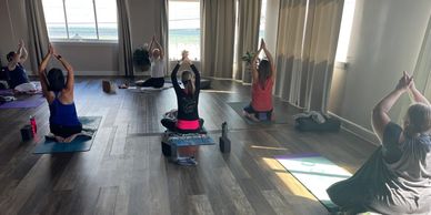 Students practicing Kundalini Yoga in Sukhasana with Anjali mudra overhead.