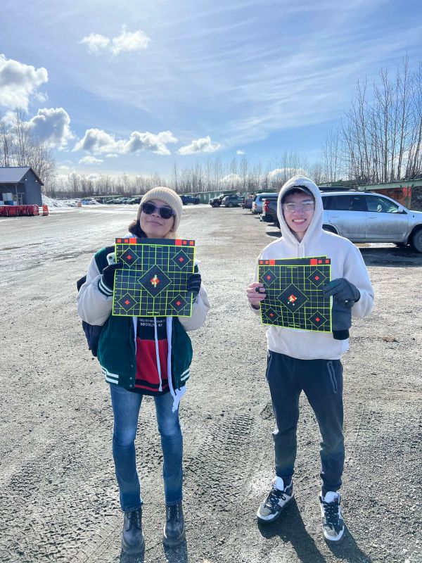 Two people outdoors holding shooting targets with bullet holes.