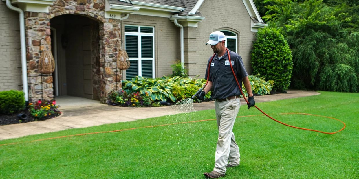 Man watering lawn with hose in front of house.
