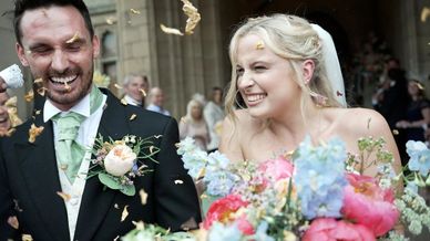 Happy bride and groom laughing as flower petals are thrown at their wedding.