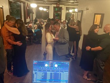Newlywed couple dancing their first dance at their wedding with the DJ in the foreground