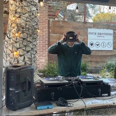 A DJ wearing headphones performs at an outdoor venue with rustic decor.