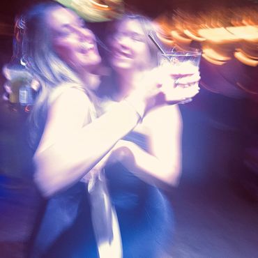 Two women dancing in the spotlight of a Dancefloor and enjoying a drink and hugging each other