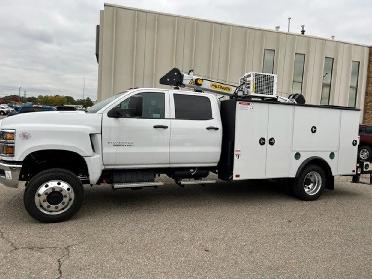 White Chevrolet Silverado 5500 HD service truck with utility compartments and crane.