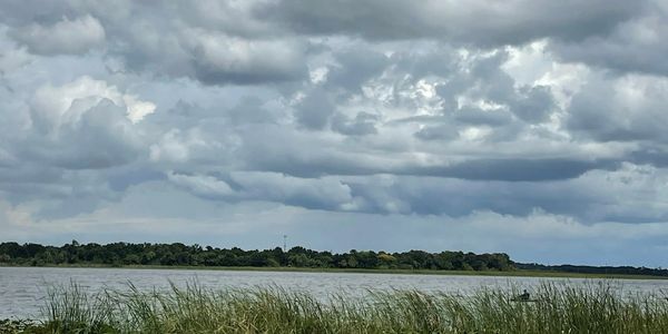 A cloudy sky over a calm river with green grass in the foreground.