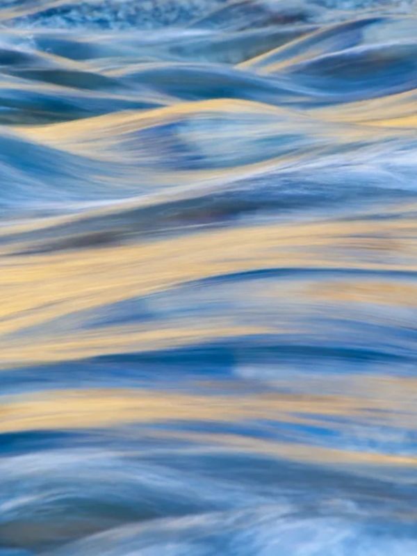 Soft waves reflecting golden sunlight on a serene water surface.
