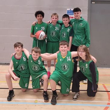 Youth basketball team posing in green uniforms on a basketball court.