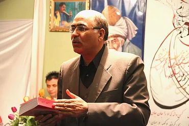 A man in a suit holding a book and speaking at an event.