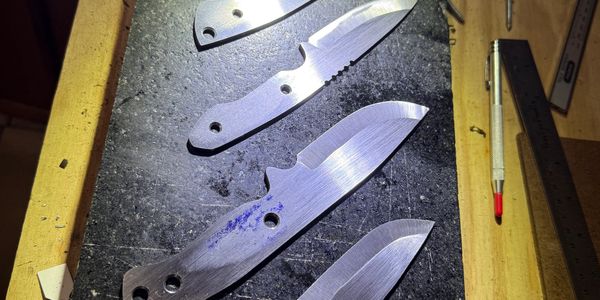 Four unfinished knife blades laid out on a workbench.